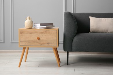 Photo of Stylish sofa with cushion and books on side table near grey wall