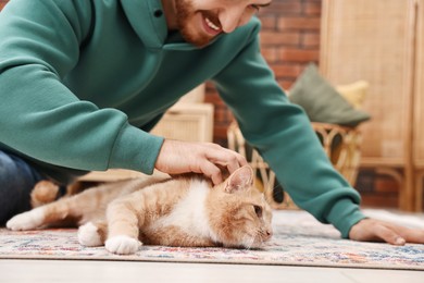 Photo of Man petting cute ginger cat on floor at home, closeup