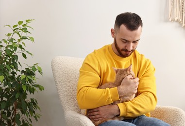 Man petting cute ginger cat on armchair at home