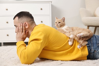 Photo of Man with cute ginger cat lying on floor at home