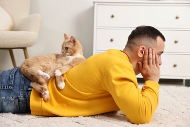 Photo of Man with cute ginger cat lying on floor at home