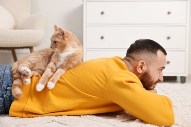 Man with cute ginger cat lying on floor at home