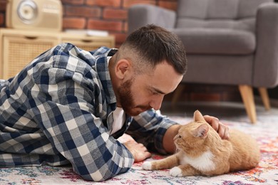 Man petting cute ginger cat on floor at home