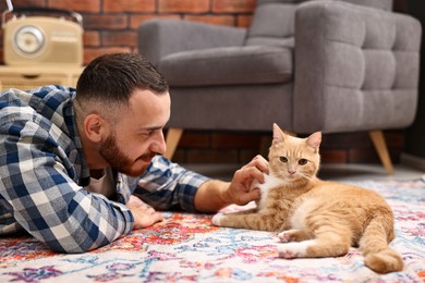 Man petting cute ginger cat on floor at home