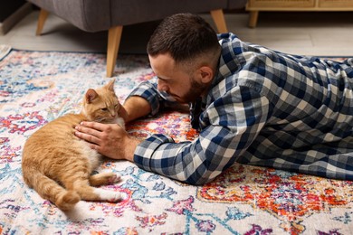 Man petting cute ginger cat on floor at home