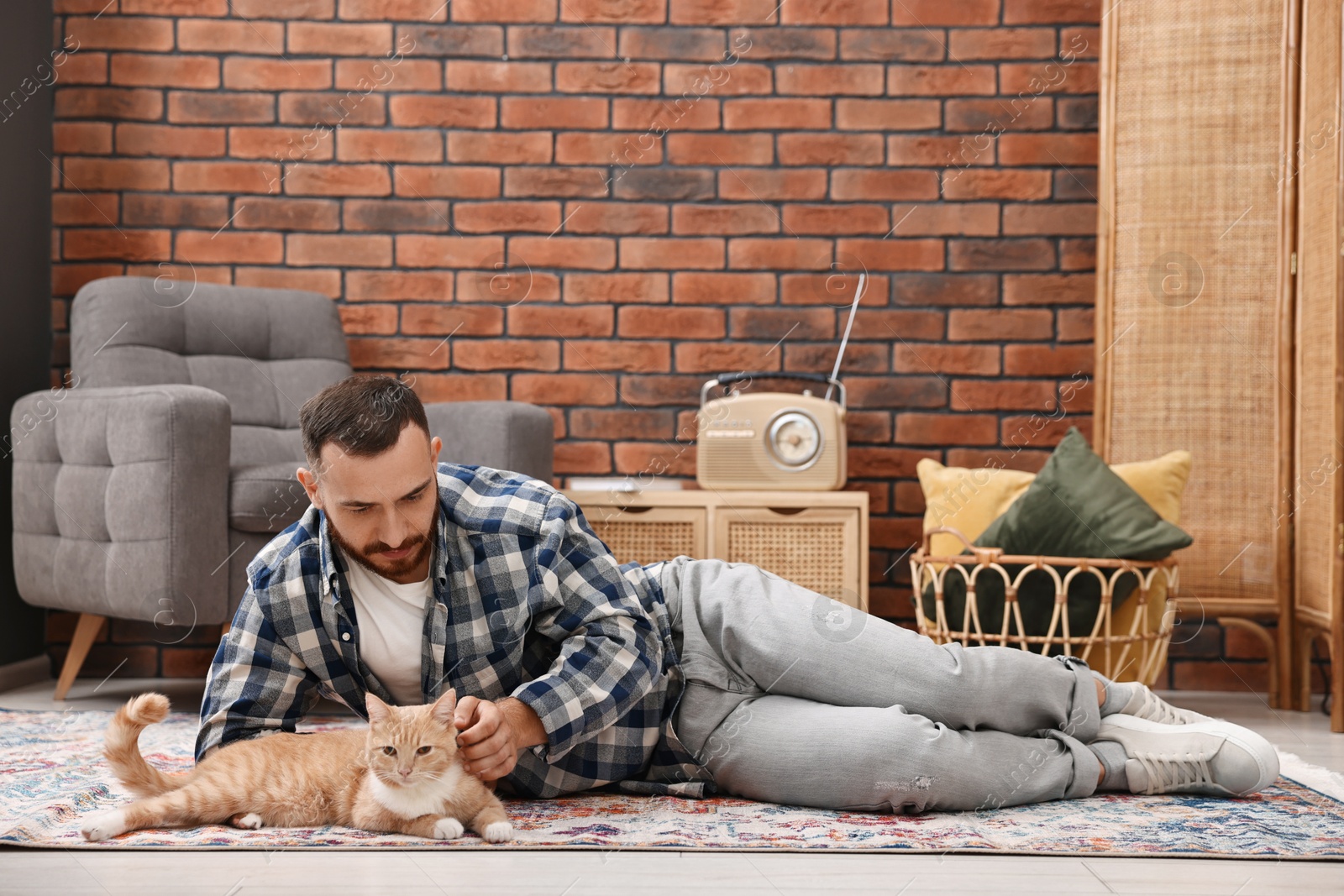 Photo of Man petting cute ginger cat on floor at home