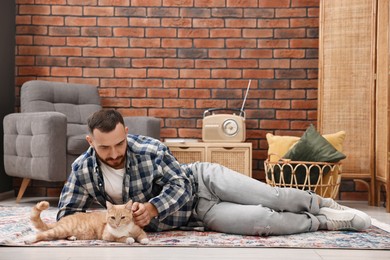 Man petting cute ginger cat on floor at home