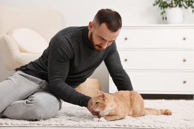 Man petting cute ginger cat on floor at home