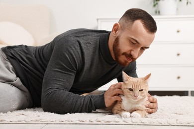 Man petting cute ginger cat on floor at home