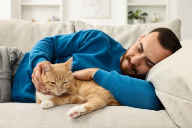 Man petting cute ginger cat on sofa at home