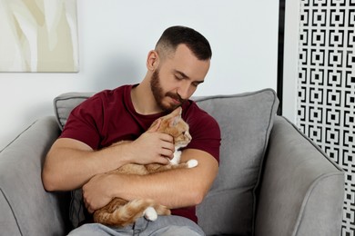 Photo of Man petting cute ginger cat on armchair at home