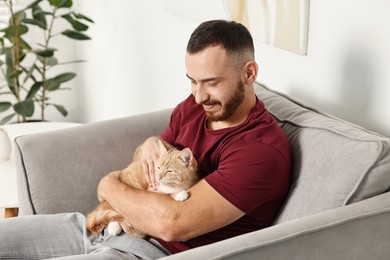 Man petting cute ginger cat on armchair at home