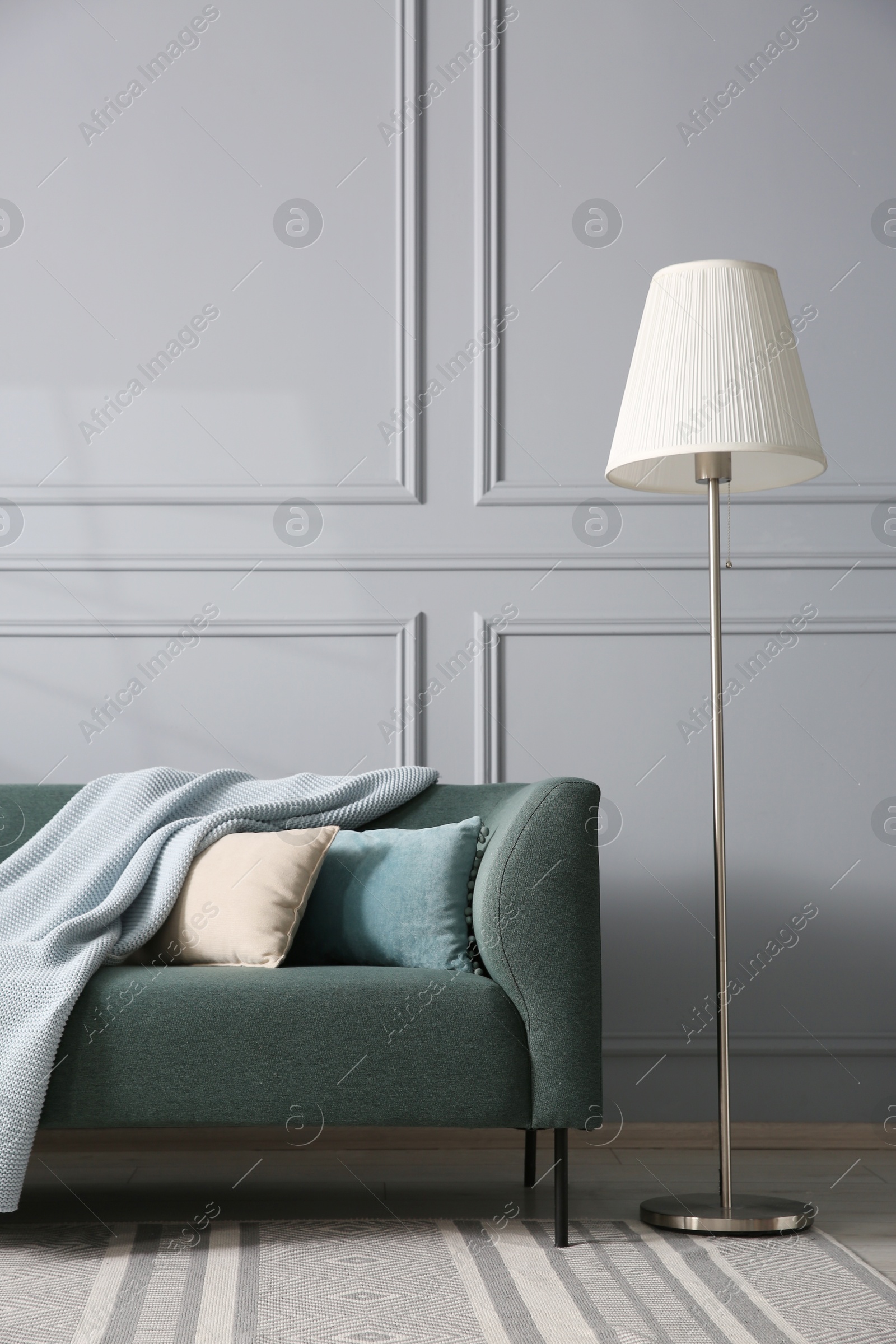 Photo of Comfortable sofa and lamp near grey wall in room