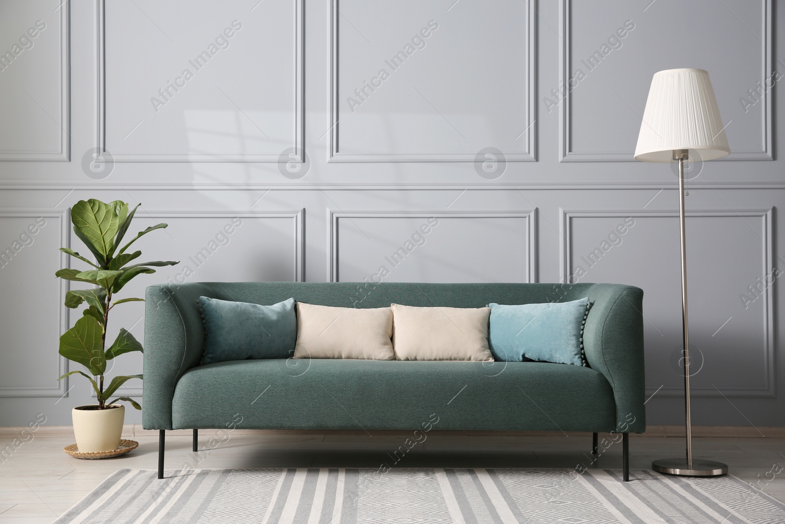 Photo of Comfortable sofa, houseplant and lamp near grey wall in room