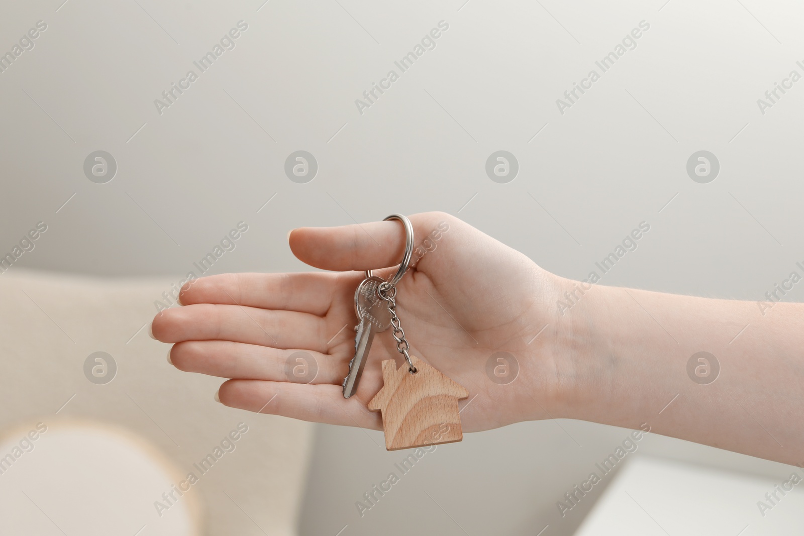 Photo of Woman holding key with house shaped keychain indoors, closeup