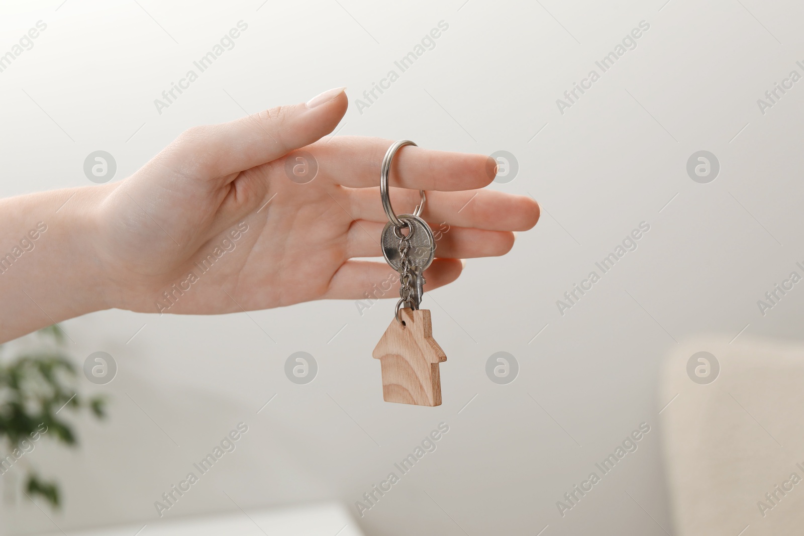 Photo of Woman holding key with house shaped keychain indoors, closeup