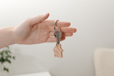 Photo of Woman holding key with house shaped keychain indoors, closeup