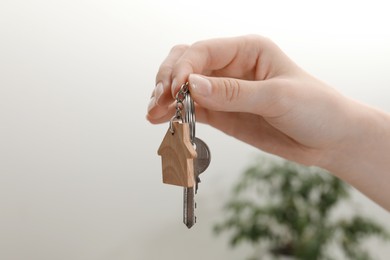 Photo of Woman holding key with house shaped keychain indoors, closeup