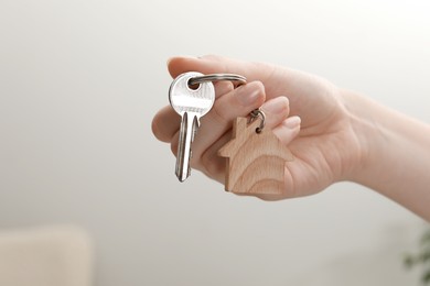 Woman holding key with house shaped keychain indoors, closeup