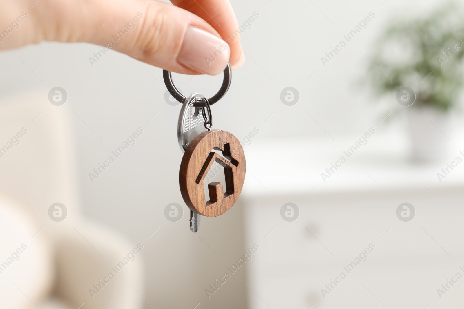 Photo of Woman holding key with house shaped keychain indoors, closeup