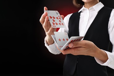 Photo of Professional croupier shuffling cards on dark red background, closeup