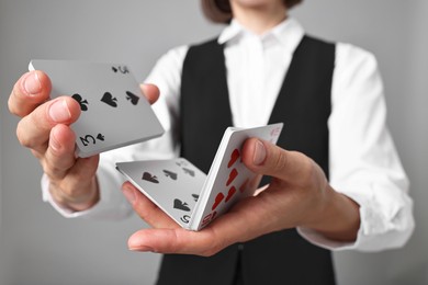 Professional croupier shuffling cards on grey background, closeup