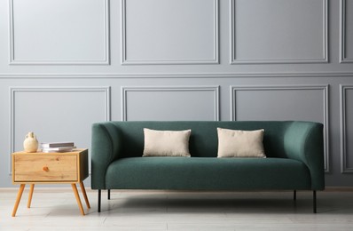 Photo of Stylish sofa with cushions and books on side table near grey wall