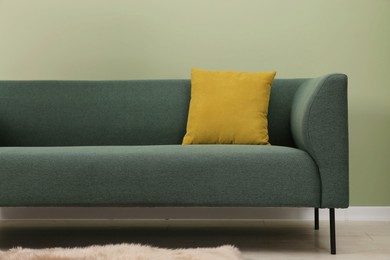 Photo of Stylish sofa with pillow near green wall indoors