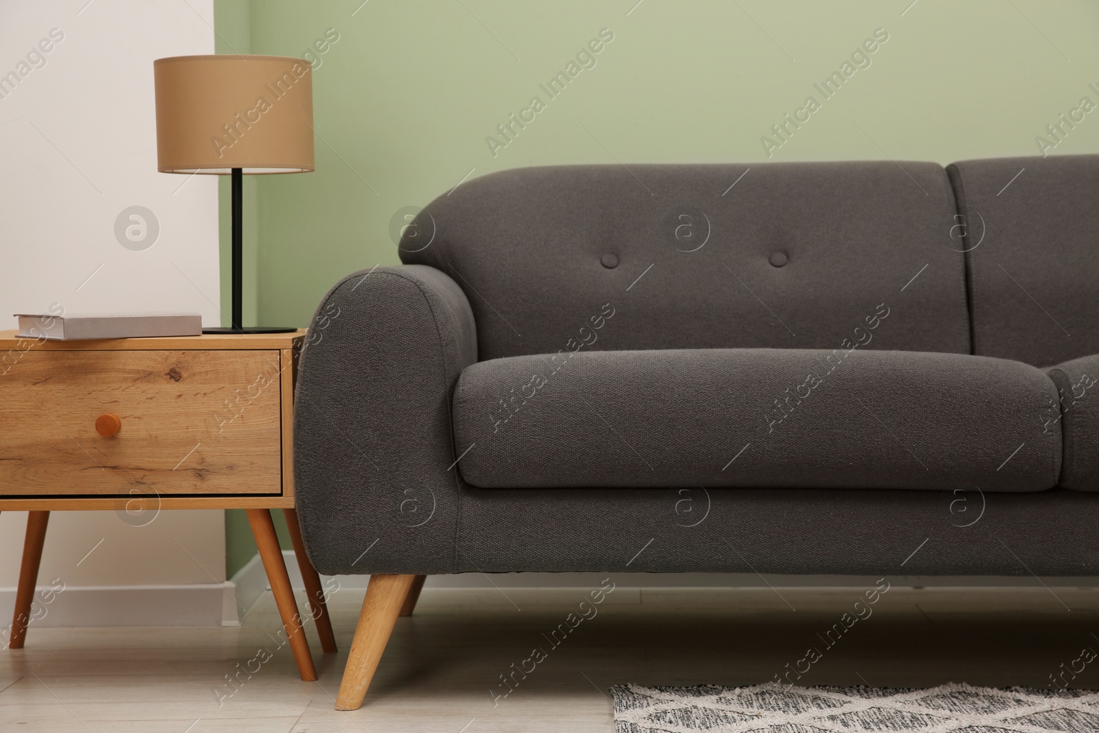 Photo of Stylish sofa, side table and lamp near green wall indoors