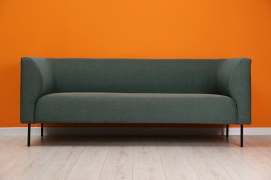 Photo of One stylish sofa near orange wall indoors