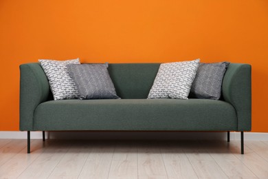 Photo of Stylish sofa with pillows near orange wall indoors