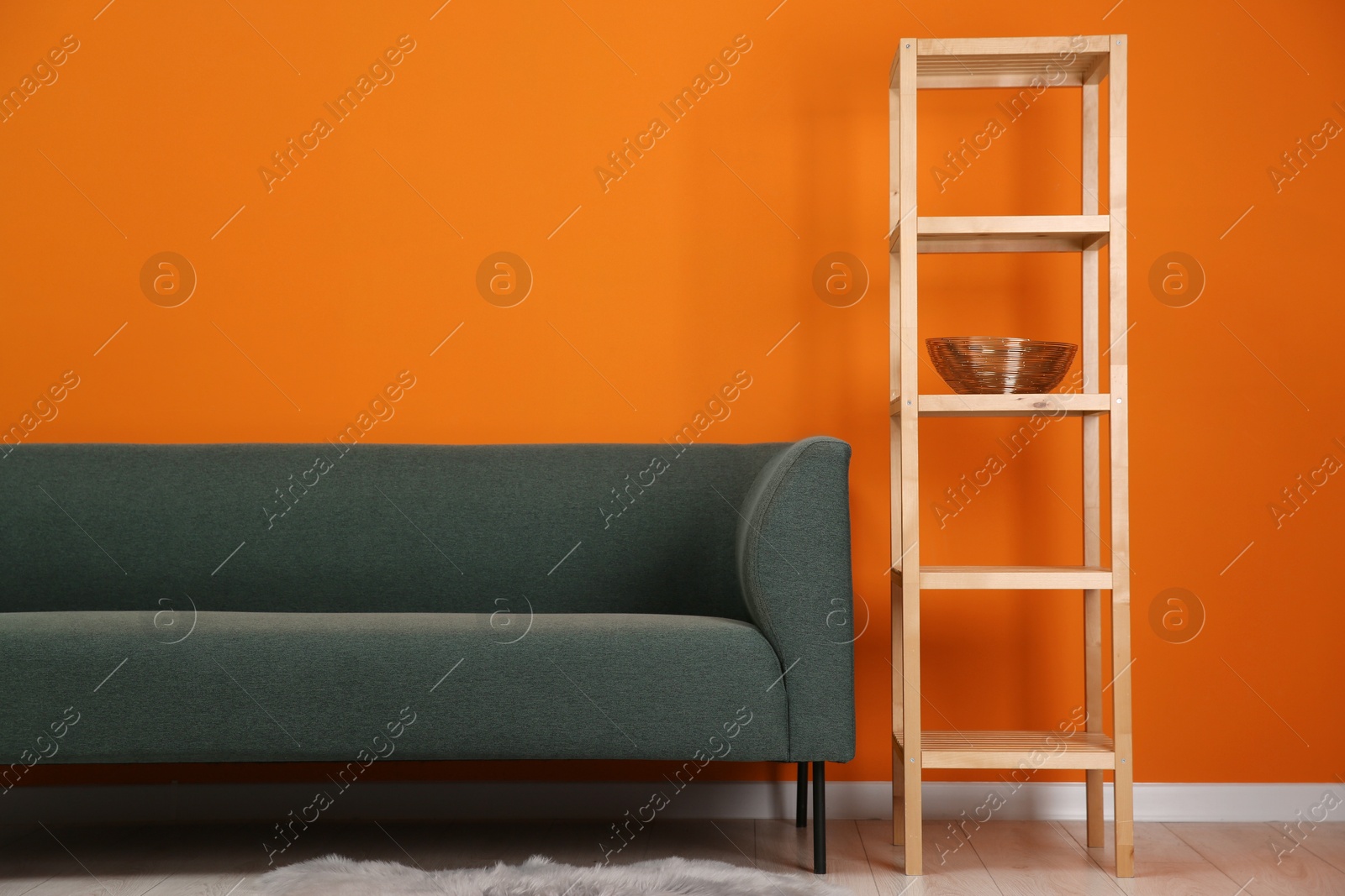 Photo of Stylish sofa and shelving unit near orange wall indoors