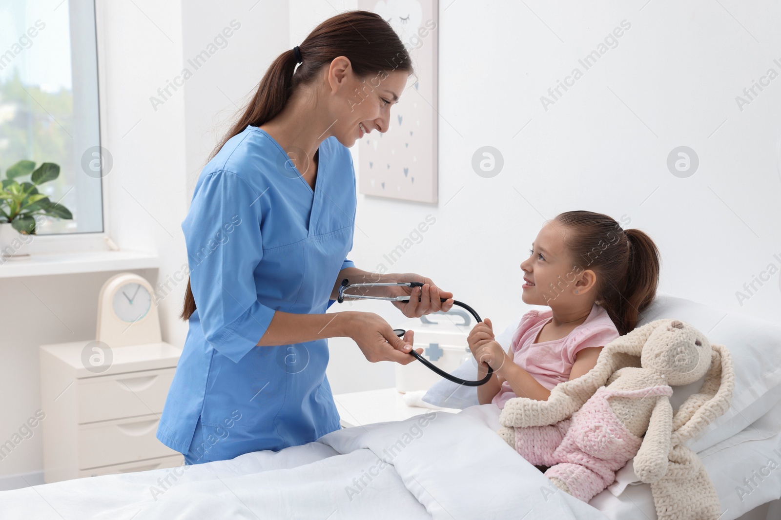 Photo of Doctor examining little girl on bed at hospital