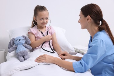 Doctor examining little girl on bed at hospital