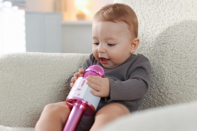 Cute little baby with microphone on armchair at home