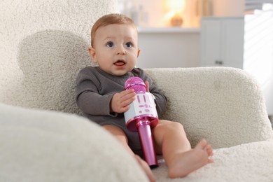 Cute little baby with microphone on armchair at home