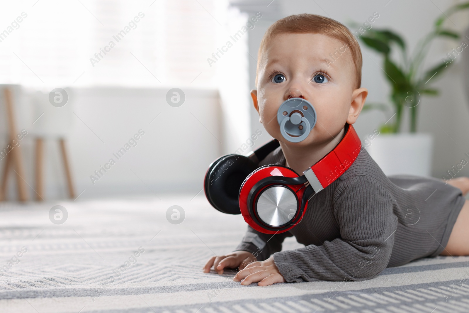 Photo of Cute little baby with pacifier and headphones on floor at home