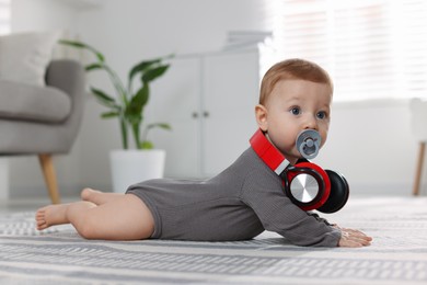 Photo of Cute little baby with pacifier and headphones on floor at home