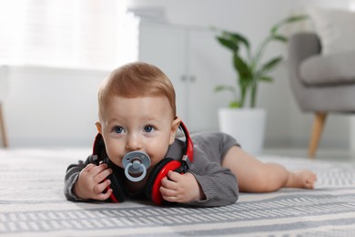 Cute little baby with pacifier and headphones on floor at home