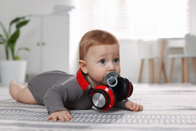 Photo of Cute little baby with pacifier and headphones on floor at home