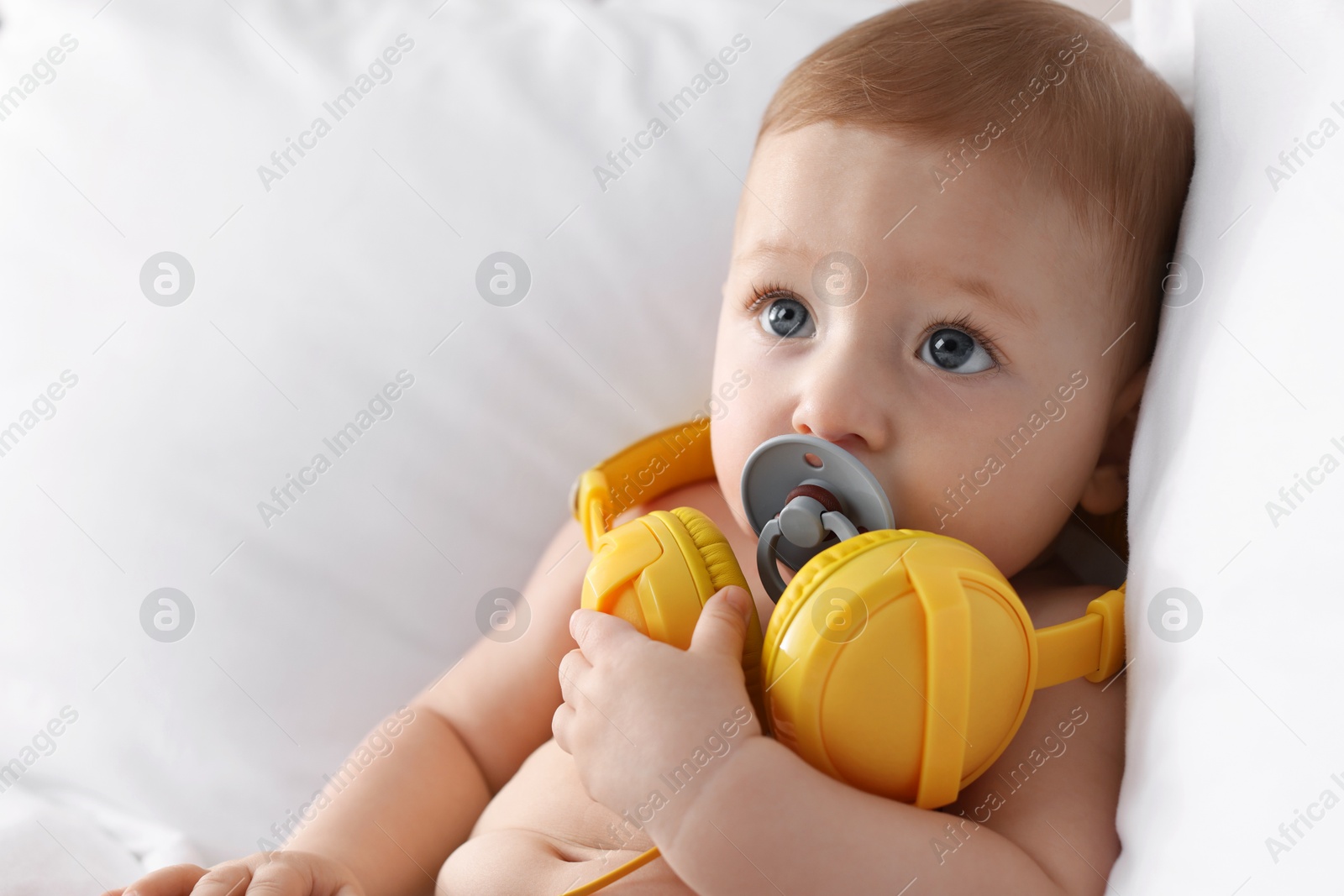 Photo of Cute little baby with headphones and pacifier on bed at home