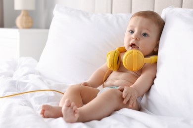 Cute little baby with headphones on bed at home, space for text