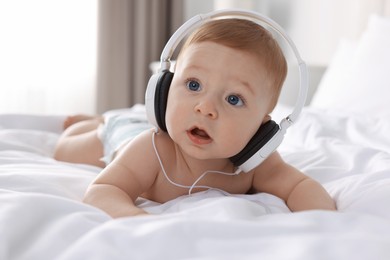 Cute little baby with headphones on bed at home