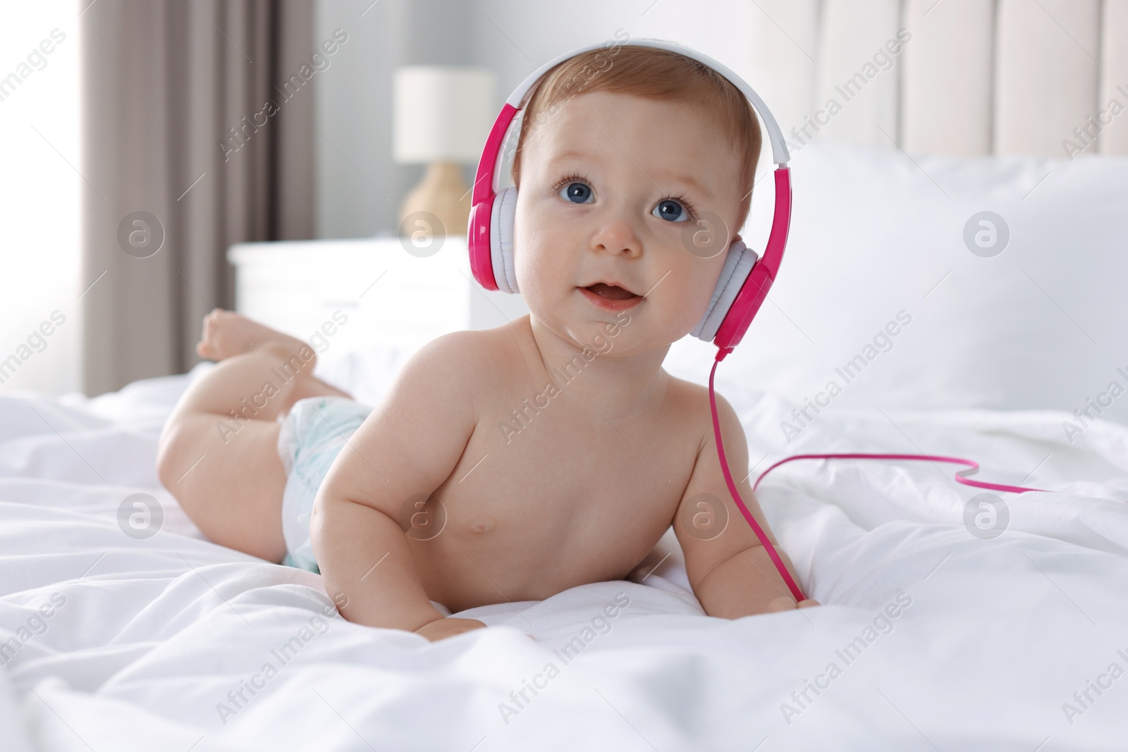 Photo of Cute little baby with headphones on bed at home