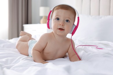 Cute little baby with headphones on bed at home