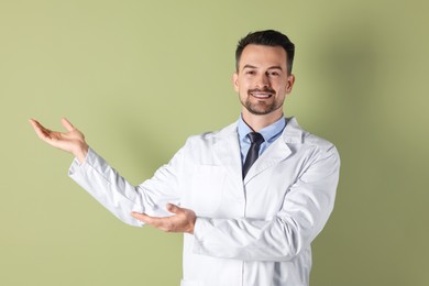 Photo of Smiling doctor pointing at something on olive background