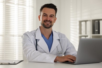 Photo of Smiling doctor working with laptop at table in clinic