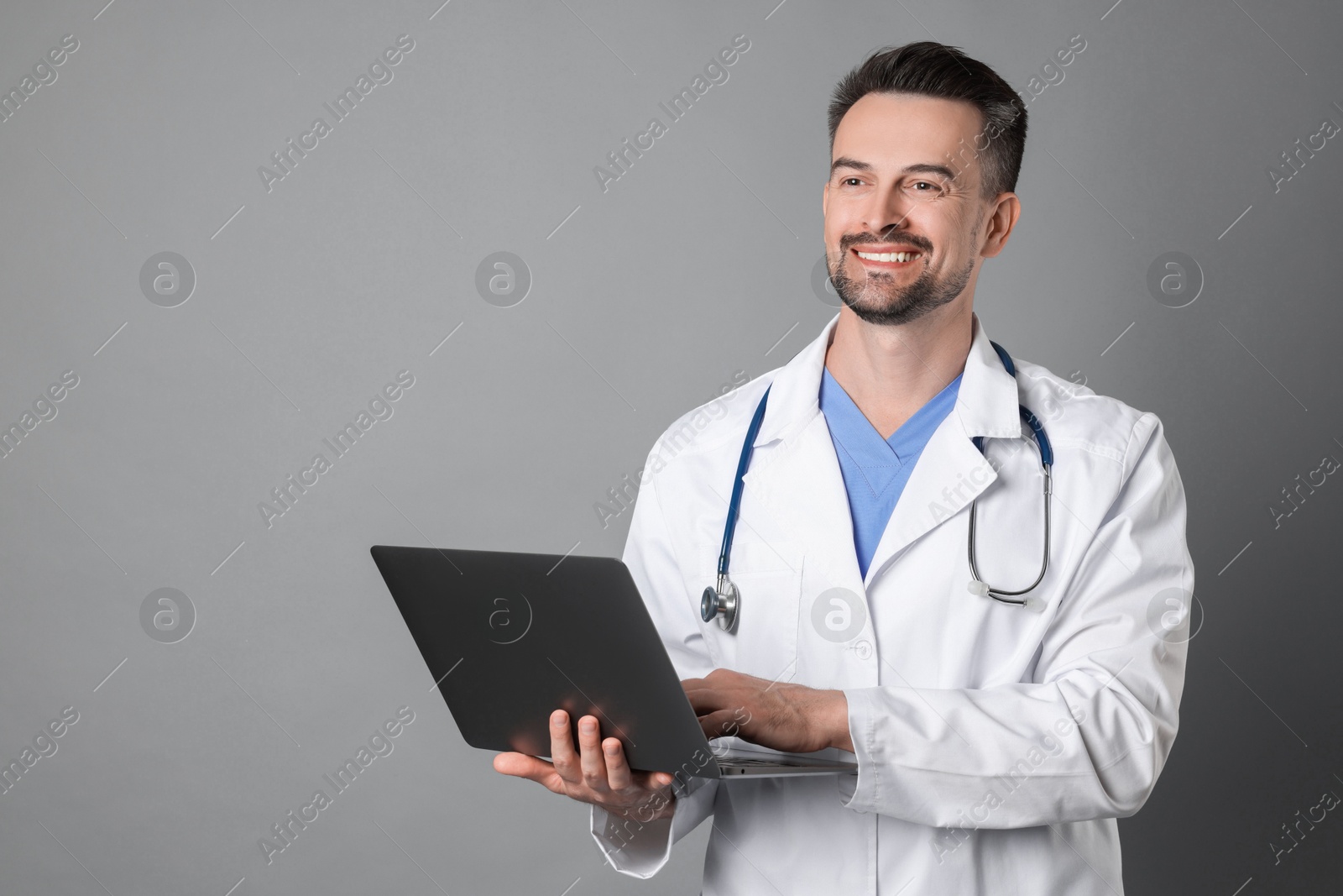 Photo of Smiling doctor with stethoscope and laptop on grey background