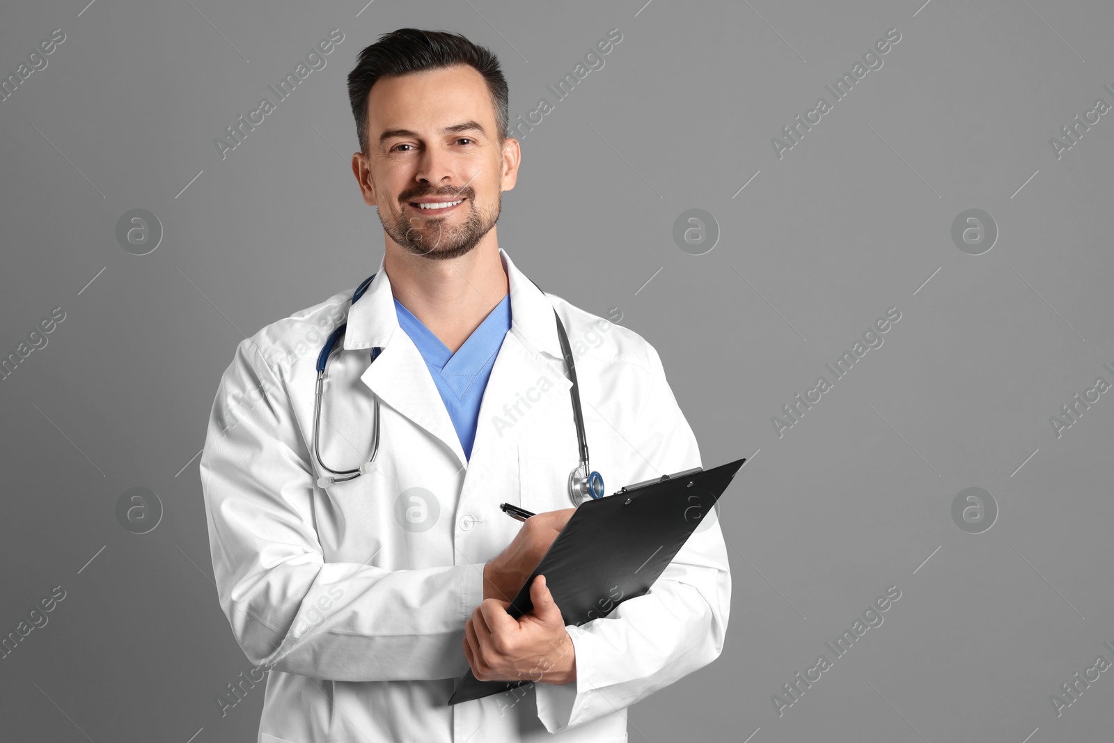 Photo of Smiling doctor with stethoscope and clipboard on grey background, space for text