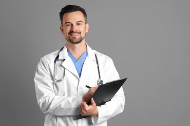 Photo of Smiling doctor with stethoscope and clipboard on grey background, space for text